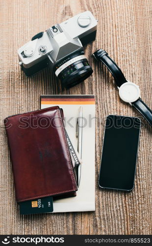 Smartphone with blank screen, camera, wallet, dollar banknotes, debit credit cards and notebook on wooden table. View from above. Portrait orientation