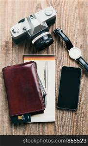 Smartphone with blank screen, camera, wallet, dollar banknotes, debit credit cards and notebook on wooden table. View from above. Portrait orientation