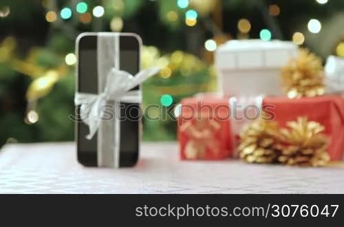 Smartphone with Christmas gifts and decorations in front of Christmas tree.