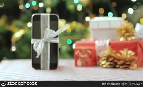 Smartphone with Christmas gifts and decorations in front of Christmas tree.