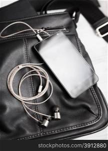 Smartphone with earphones on black leather bag.