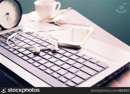 Smartphone with earphones on laptop, Coffee cup on workspace desk