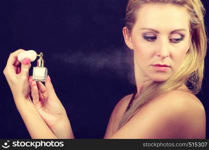 Smell, elegance concept. Beautiful elegant blonde woman with necklace applying perfume after shower on naked body, studio shot on dark background. Beautiful woman with holding and applying perfume