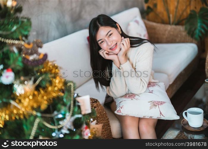 smile happiness portrait beautiful young asian woman wearing warm clothes sitting on the sofa with coffee cup mug Decoration During Christmas x-mas and New Year holidays at home in room inside or cafe