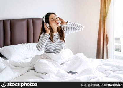 Smile happy young asian woman relaxing and using headphones to listen to music from smart phone in bedroom