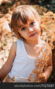 Smile portrait little caucasian baby girl squatting in the forest among ferns observes plants
