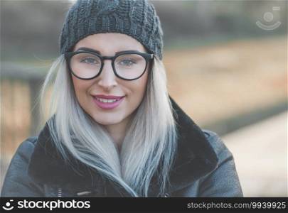 Smile woman face in snowflakes on winter day outdoors. Closeup cute girl wearing warm wool cap and black jacket. Female person in cold weather.