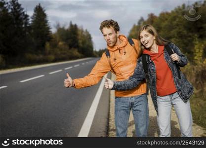 smiley couple hitchhiking while road trip