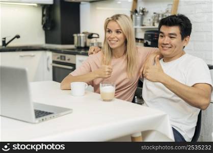 smiley couple home during pandemic giving thumbs up while looking laptop
