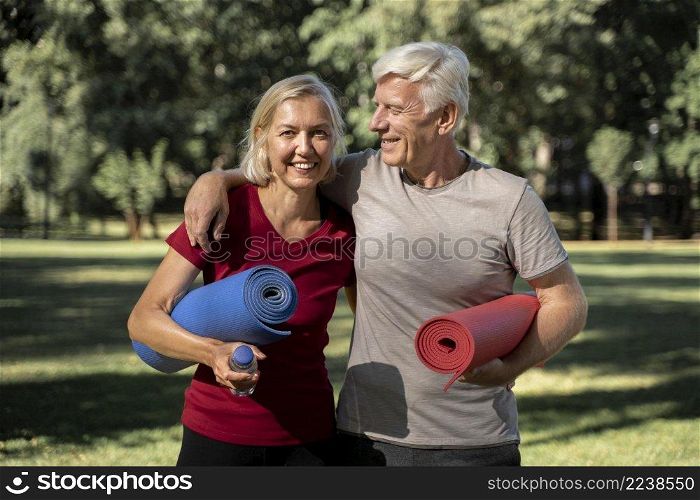 smiley elder couple outdoors with yoga mats water bottle