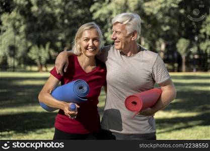 smiley elder couple outdoors with yoga mats water bottle