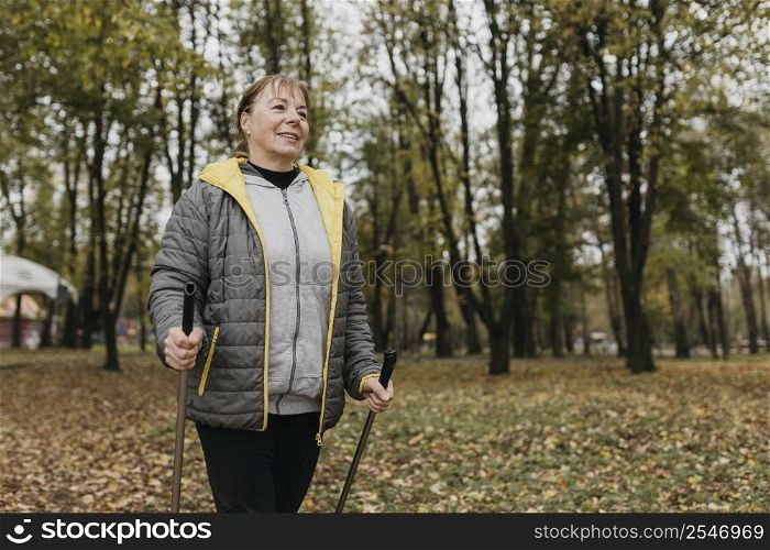 smiley elder woman with trekking sticks outdoors copy space