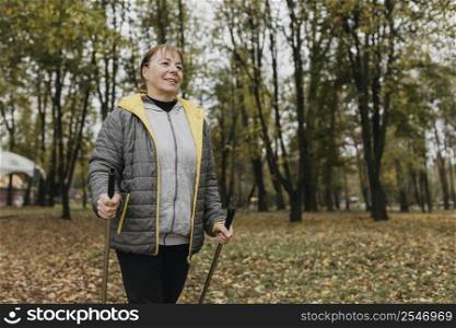 smiley elder woman with trekking sticks outdoors copy space