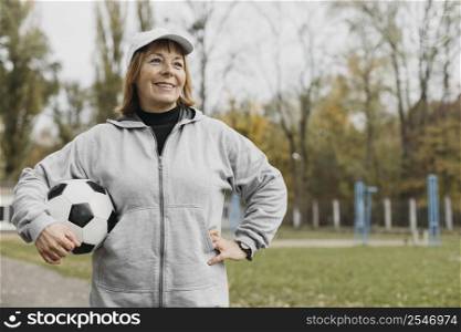 smiley elderly woman holding football outdoors while working out