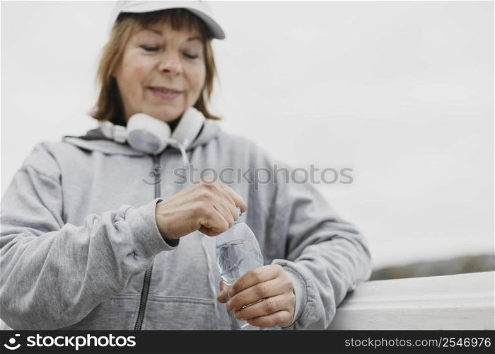 smiley elderly woman with water bottle headphones outdoors