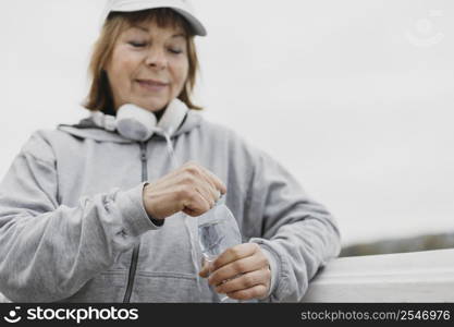 smiley elderly woman with water bottle headphones outdoors