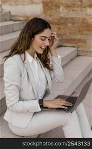 smiley elegant businesswoman with smartwatch working laptop outdoors