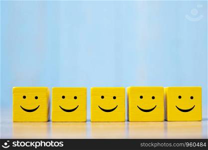 smiley face on yellow wood cube. Service rating, ranking, customer review, satisfaction and emotion concept.
