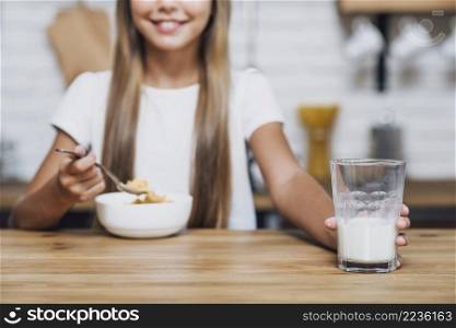 smiley girl holding glass milk while eating cereal