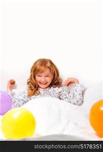Smiley little girl in bed surrounded by coloured ballon