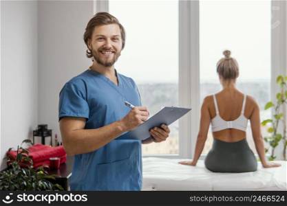 smiley male osteopathic therapist with clipboard female patient clinic
