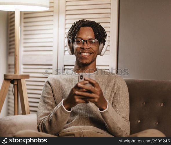smiley man home couch using smartphone headphones
