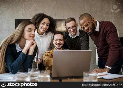 smiley man showing something his colleagues laptop during meeting