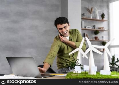 smiley man working eco friendly wind power project while talking phone using laptop