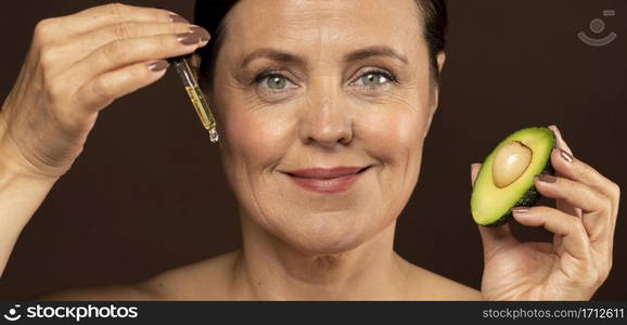 smiley mature woman holding half avocado with serum