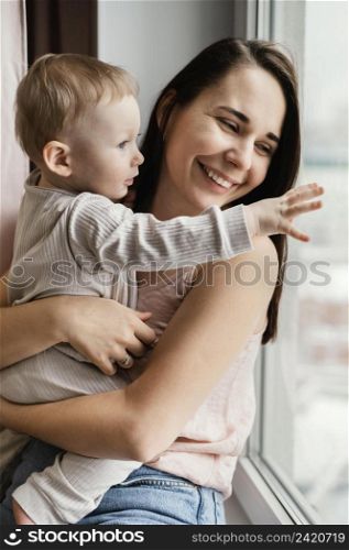 smiley mother holding her child close window