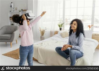 smiley mother watching daughter play with virtual reality headset