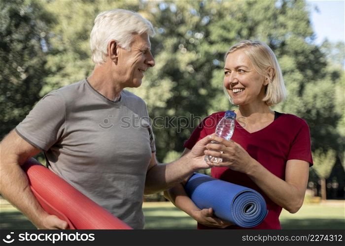 smiley older couple outdoors with yoga mats water bottle