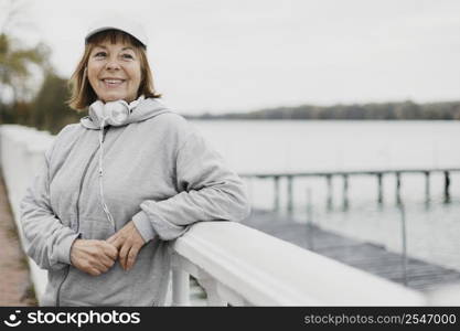 smiley older woman posing outdoors with headphones while working out
