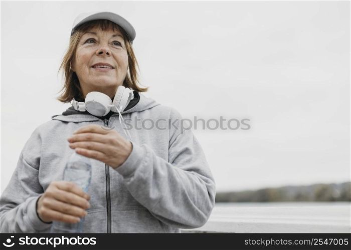 smiley older woman with water bottle headphones outdoors