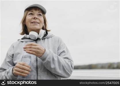 smiley older woman with water bottle headphones outdoors