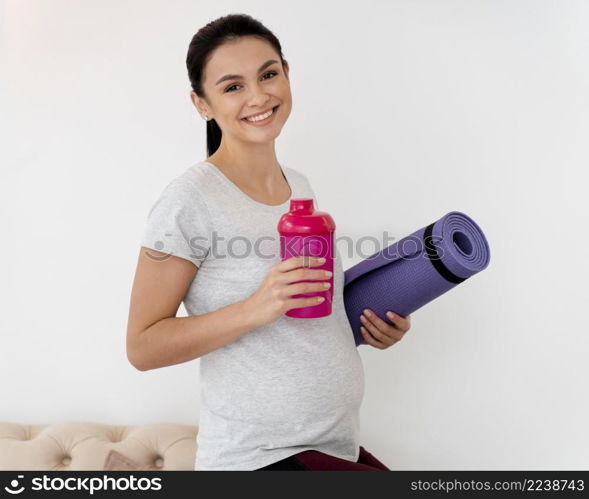 smiley pregnant woman holding fitness mat bottle water