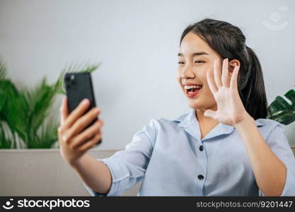 Smiley pretty teenage sitting on sofa and use smartphone to video call or selfie,  during quarantine covid-19 self isolation at home