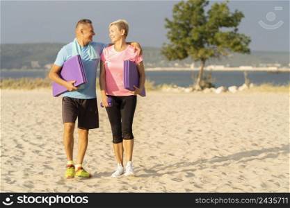 smiley senior couple with working out equipment beach copy space