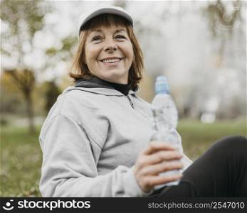 smiley senior woman drinking water outdoors after working out