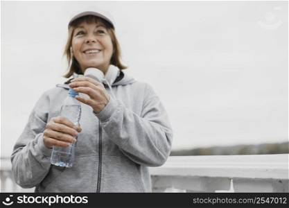smiley senior woman with water bottle headphones outdoors