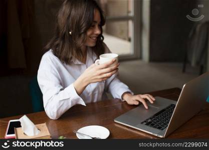 smiley woman holding cup coffee working laptop
