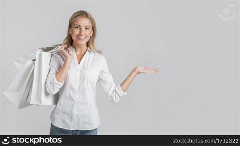 smiley woman holding shopping bags showing off space her left