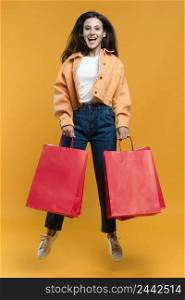 smiley woman posing while jumping holding shopping bags