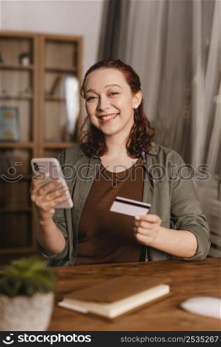 smiley woman using credit card smartphone home
