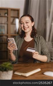 smiley woman using credit card smartphone home