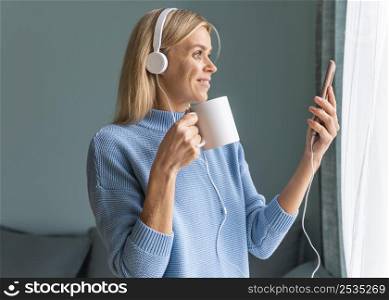 smiley woman using smartphone headphones home while having coffee during pandemic