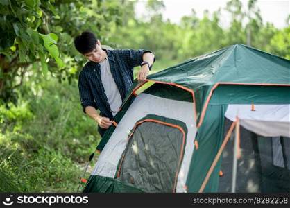 Smiley Young traveler man setting a tent on the c&ing in the forest on summer vacation
