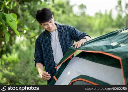 Smiley Young traveler man setting a tent on the c&ing in the forest on summer vacation