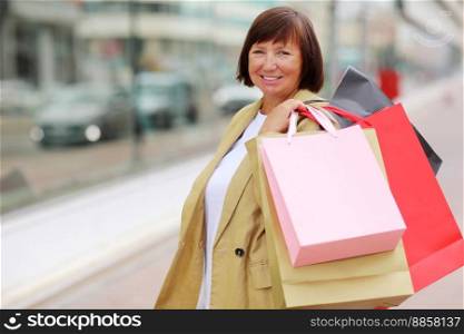 Smiling adult woman with shopping bags. Middle ages female after shopping on shopping mall background. Purchases, black friday, discounts, sale concept. Online shopping concept, Seasonal Sales.mockup. Smiling adult woman with shopping bags. Middle ages female after shopping on shopping mall background. Purchases, black friday, discounts, sale concept. Online shopping concept, Seasonal Sales. mockup