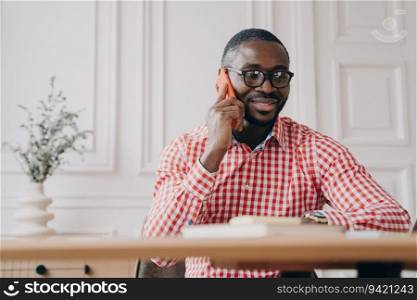 Smiling African American businessman consulting client, talking on mobile in office; dark-skinned male worker making call.